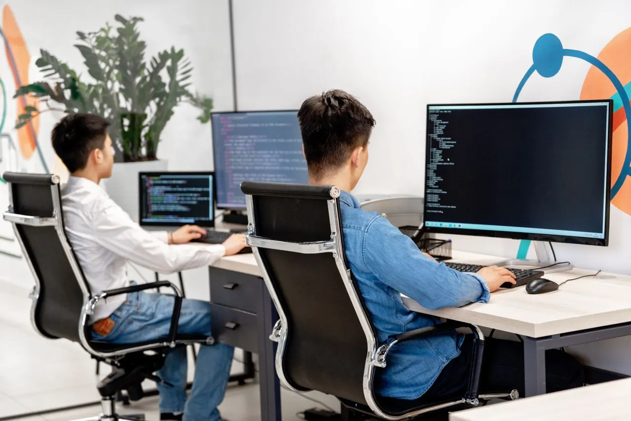 Two developers working at dual-monitor desks in the AI Pineal office